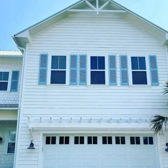 Clean, white two-story house exterior with blue shutters and a garage. Ideal for pressure washing Wilmington NC services.