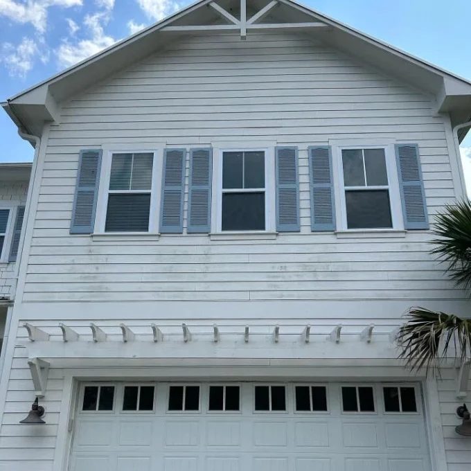 White house exterior with slight discoloration. Blue shutters and a garage door below suggest need for pressure washing Wilmington NC.