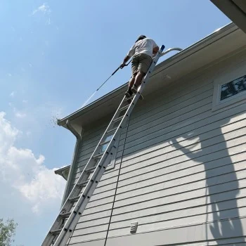 Person on ladder pressure washing home siding under clear sky, emphasizing pressure washing Wilmington NC services.