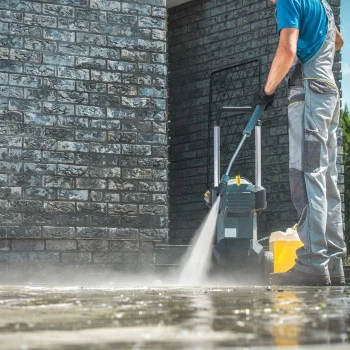 New Construction Worker pressure washing a stone surface in Wilmington NC, using a high-powered spray to clean dirt from the ground next to a brick wall.