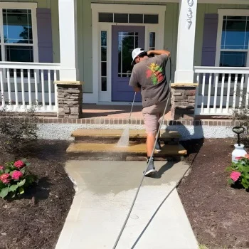 Porch & Concrete Cleaning (2) Person pressure washing a home's front steps in Wilmington, NC, surrounded by a well-kept garden with blooming flowers.