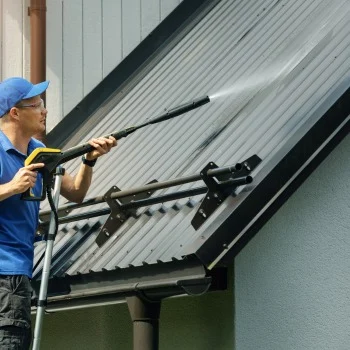 Person in blue uses a pressure washer to clean a metal roof. Ideal for pressure washing Wilmington NC needs.