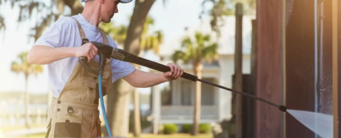 Man pressure washing a wooden wall in a sunny yard, highlighting pressure washing Wilmington NC services.