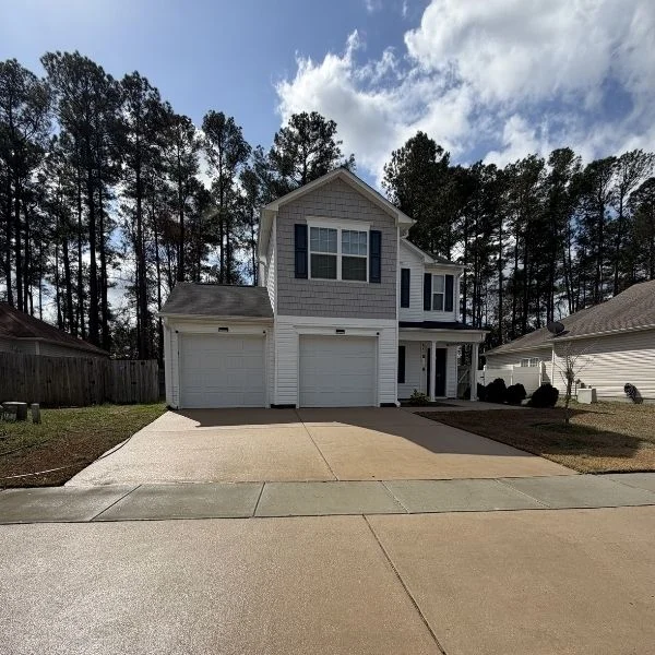 Two-story house with clean driveway, surrounded by tall trees, highlighting results of pressure washing Wilmington NC.