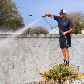 Man pressure washing a textured wall, standing on a stump, wearing casual attire in Wilmington NC.
