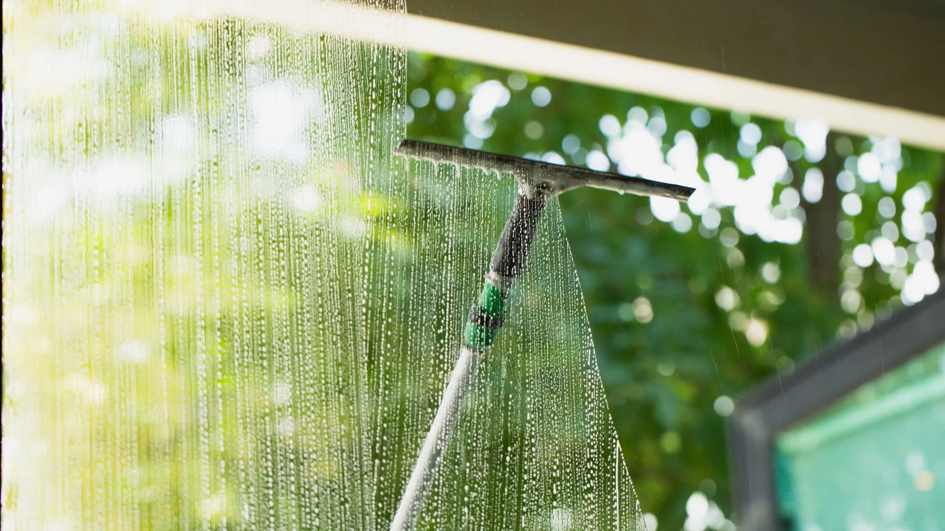 Squeegee clearing water streaks from a window with trees blurred outside, showcasing pressure washing Wilmington NC.