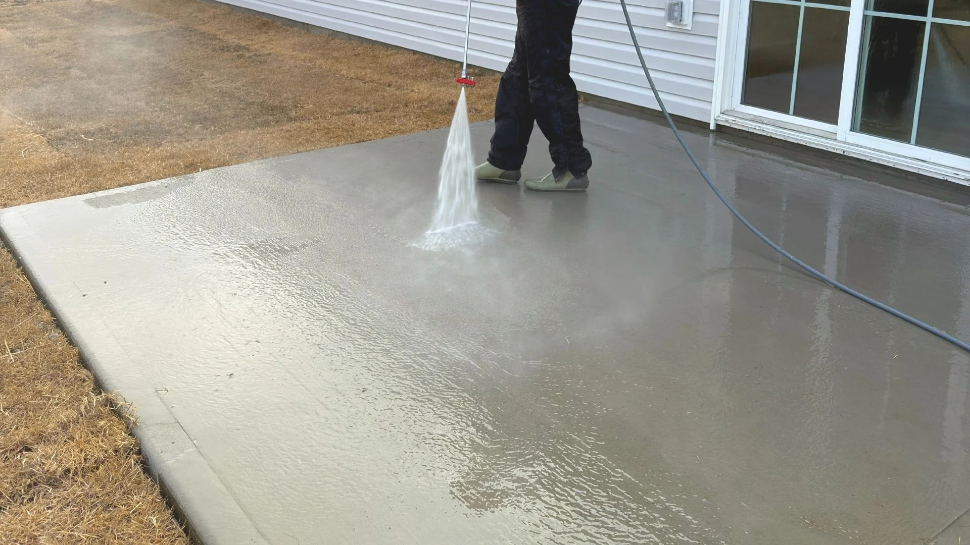 Person pressure washing a concrete patio near a house, creating a cleaner surface, emphasizing pressure washing services in Wilmington NC.
