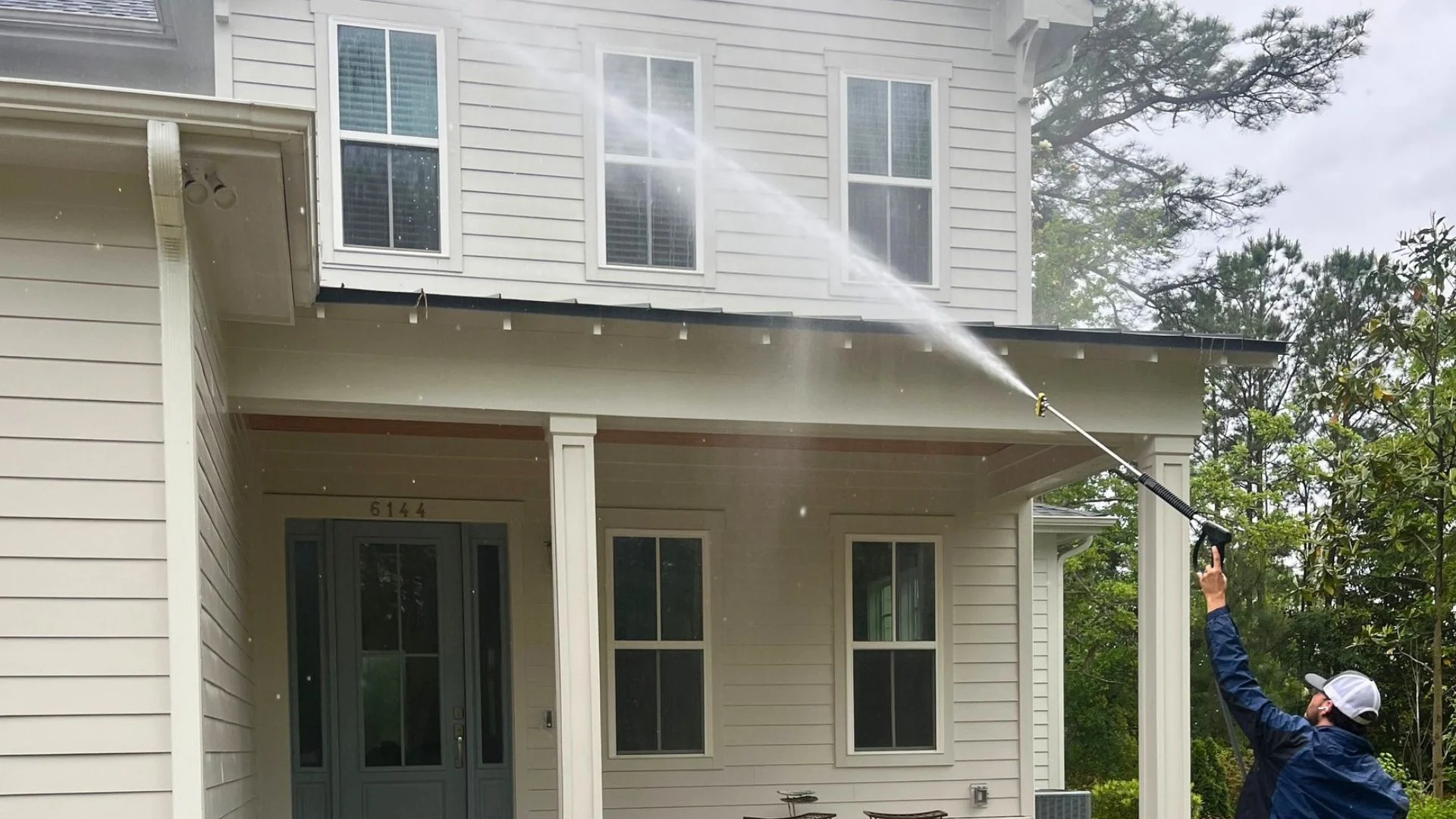 Worker pressure washing Wilmington NC house exterior, spraying water onto the upper facade of a two-story home.